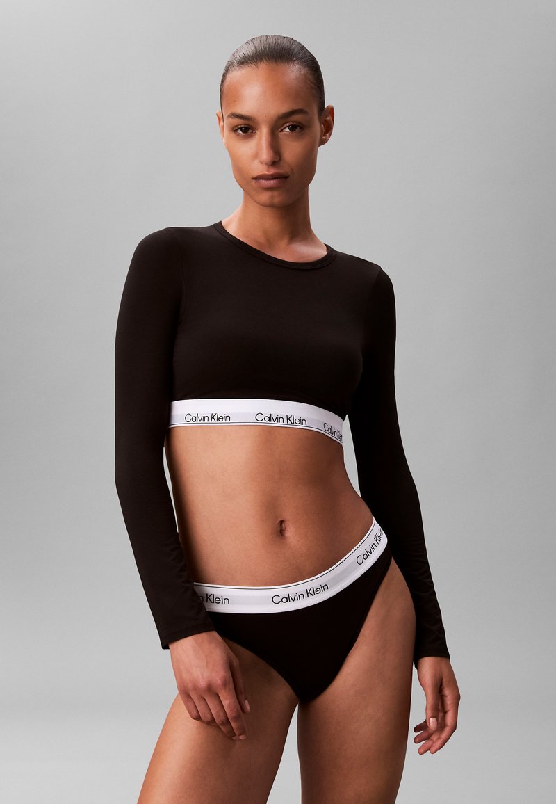 Black long-sleeve crop top with a white "Calvin Klein" logo band; matching black bikini bottoms with a similar band around the waist.