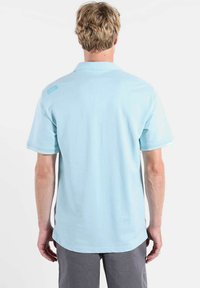 Polo bleu clair avec une texture douce, manches courtes et ourlet droit. Dispose d'une petite étiquette logo dans le haut du dos.