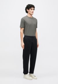 Tricou gri texturat cu mâneci scurte, asortat cu pantaloni negri plisati și pantofi sport bej, având croială lejeră și talie elastică.