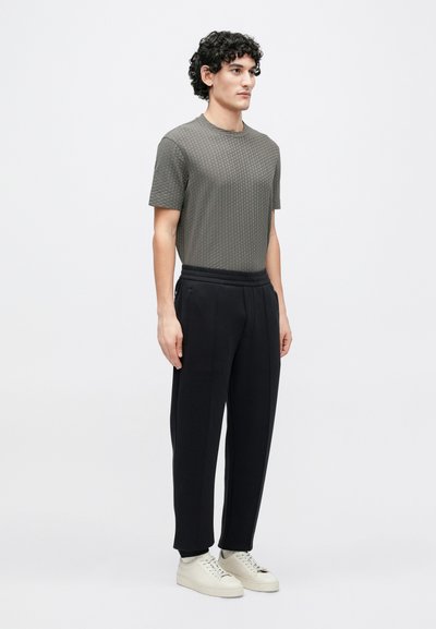 Trumpomis rankovėmis, tekstūruota pilka palaidinė, derinama su juodais klostuotais kelnėmis ir smėlio spalvos sportbačiais, pasižymi laisvu siluetu ir elastine juosmens juosta.