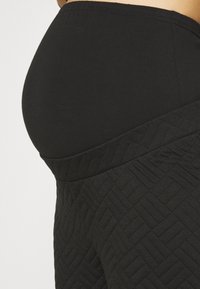 Svarta gravidyogabyxor med ett texturerat, quiltat mönster. Midjebandet är brett och slätt, utformat för komfort och stöd.
