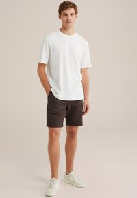 Witte t-shirt met korte mouwen en textuur, gecombineerd met donkerbruine shorts en witte sneakers, met een relaxte pasvorm en casual ontwerp.