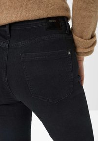 Jeans in denim nero con una texture liscia, dotati di una tasca posteriore, cuciture sottili e un'etichetta in pelle sul girovita.