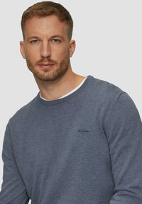 Zils džemperis no mīksta auduma ar apaļu kakla izgriezumu un redzamām šuvēm. Uz krūtīm ir neliels melns "s.Oliver" logo.