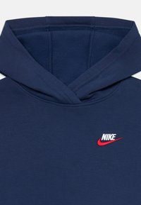 Hanorac bleu inchis cu o textură moale, dotat cu un logo Nike brodat roșu pe partea stângă a pieptului și un design cu glugă dublă.