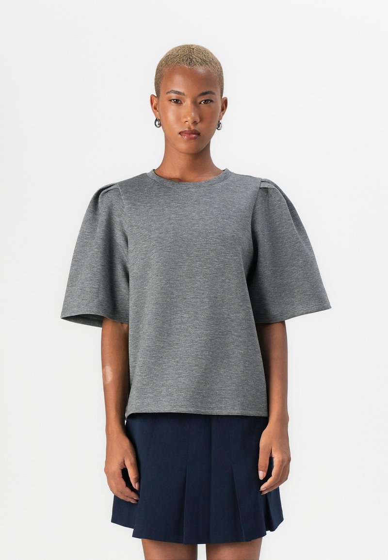Pullover grigio a maniche corte con scollo rotondo e maniche puff, realizzato in tessuto morbido, abbinato a una gonna plissettata blu scuro.