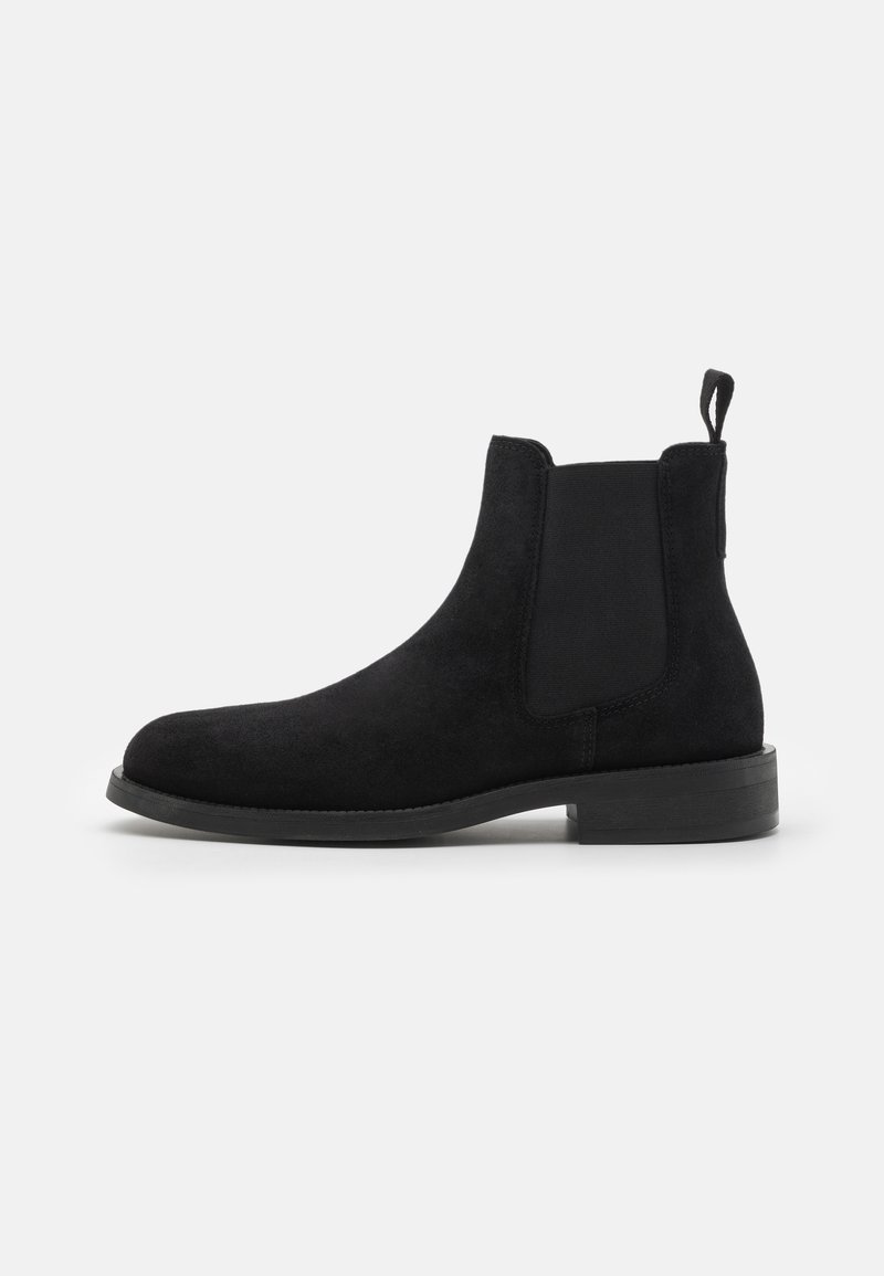 Schwarze Wildleder-Ankle Boots mit elastischen Seitenpaneelen, runder Zehenform, Zugschlaufe und niedrigem, gestapeltem Absatz. Sanfte Textur und minimalistisches Design.