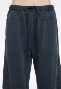 Temno sivi sweatshirt hlače z elastičnim pasom, vrvico in stranskimi žepi. Mehka tekstura in sproščen kroj, primerne za vsakodnevno nošenje.