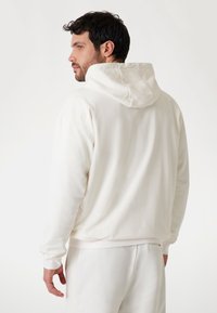Weiße Kapuzenjacke mit strukturiertem Muster, gerippten Bündchen und Saum. Die Rückseite hat eine Nahtdetail und eine lockere Passform.