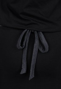 Czarny top z tkaniny z wiązaniem w talii w ciemniejszym odcieniu szarości, tworzący dopasowany kształt. Miękka tekstura.