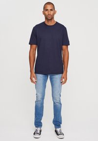 Navy cotton t-shirt with short sleeves, paired with light blue slim-fit jeans and black and white sneakers. Simple, casual design.