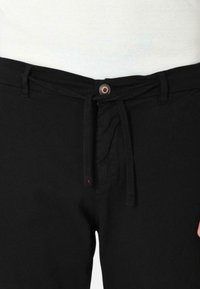 Pantaloni neri con cordoncino e chiusura a bottone, caratterizzati da una texture liscia e cuciture sottili. Progettati per comodità e versatilità.