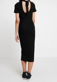 Robe midi noire à côtes avec un dos découpé et un détail de lien, dotée de manches courtes. Associée à des baskets noires pour un look décontracté.