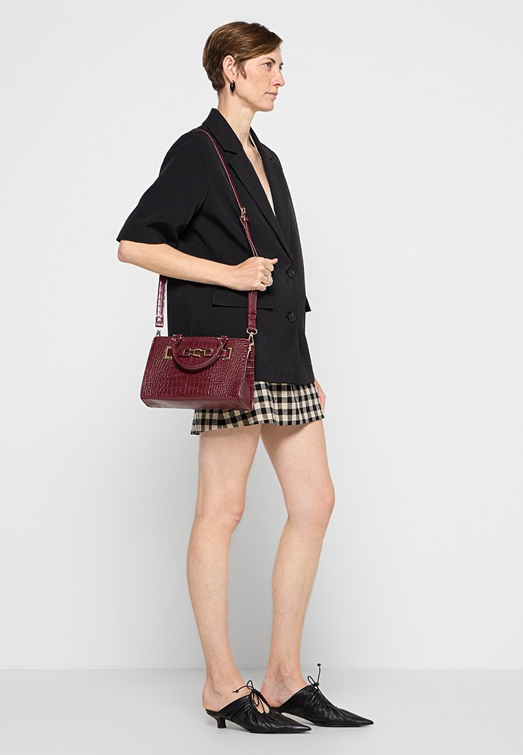 Sac à main en crocodile bordeaux avec une poignée supérieure et une bandoulière réglable. Présente des accents en métal doré et une forme rectangulaire.