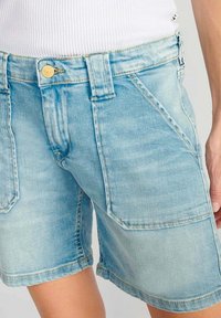 Shorts en denim bleu clair avec une texture déchirée, dotés d'une fermeture à bouton, de poches avant et d'une coupe légèrement ample.