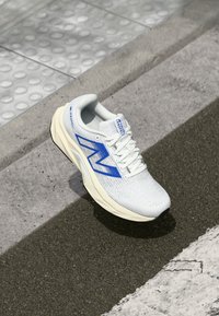 Baskets blanches avec des accents bleus, dessus en maille texturée et semelle rembourrée. Présente un logo "N" bien visible sur le côté.