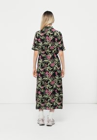 Robe midi florale noire avec des feuilles vertes et des orchIdées roses. Manches courtes, ceinture à la taille et une silhouette droite associée à des baskets.
