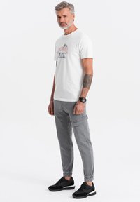 Witte katoenen t-shirt met een grafische print, gecombineerd met grijze cargobroeken met zakken en elastische boorden, afgewerkt met zwarte sneakers.