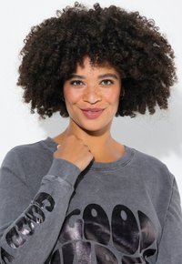 Sweatshirt gris à manches longues, avec un texte métallique noir sur le devant. Tissu doux et texturé avec des poignets côtelés visibles.