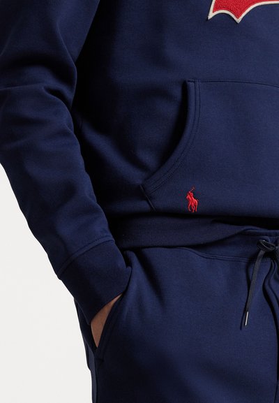 Sudadera de color azul marino con un logo bordado en rojo, bolsillo tipo canguro, puños acanalados y cintura con cordón. Tejido suave de mezcla de algodón.