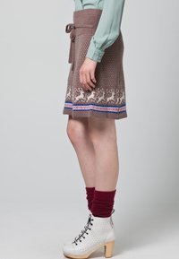 Jupe en tricot marron avec un motif de renne au bas, accentuée de rayures bleues et rouges. Associée à des bottes blanches à lacets et des chaussettes bordeaux.