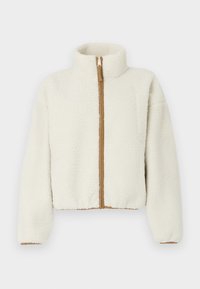 Jakna od flisa u krem boji s visokim ovratnikom, prednjim patentnim zatvaračem i kontrastnim smeškim patentnim zatvaračem. Ima skraćen, kutijasti oblik i teksturirani materijal.