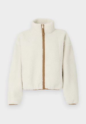 Giacca in pile color crema con colletto alto, chiusura con zip e zipper marrone a contrasto. Presenta una forma cropped e squadrata e un tessuto testurizzato.