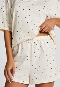 Katoenen loungewearset met een losvallende top met korte mouwen en shorts met elastische tailleband, beide met zwarte stippen op een crèmekleurige achtergrond.