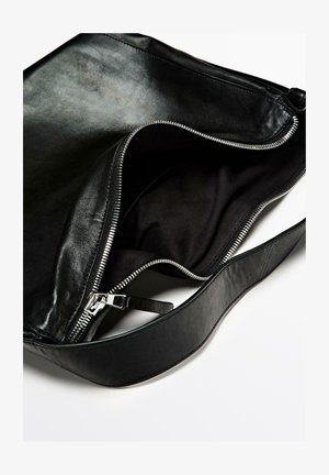 Zwarte leren tas met een ritsluiting en een gladde textuur. Beschikt over een brede schouderband en een ruime, donkere stoffen binnenkant.