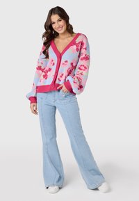 Blommönstrad cardigan i blått och rosa med V-ringning, knappstängning och vida ärmar, kombinerad med ljus denim i utsvängd modell och vita skor.