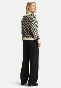 Black and cream patterned sweater with a zigzag design, featuring a soft texture and fitted waist, paired with wide-leg black pants.