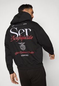 Black hoodie with large white and red text on the back, featuring a circular emblem and "Sport Lisboa e Benfica" text. Soft fabric, relaxed fit.