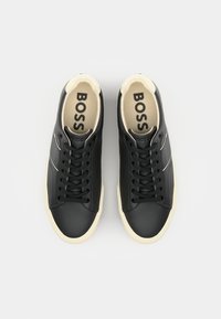 Adidași negri din piele cu o textură specială, având o talpă din gumă de culoare crem, șireturi negre și un branding discret pe limbă și pe lateral.