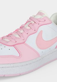 Close-up van een witte en roze Nike-sneaker met roze veters en een roze Nike-swoosh aan de zijkant.