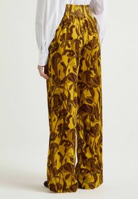 Pantaloni a gamba larga in tessuto color giallo senape con stampa floreale in tonalità marroni. La cintura presenta un design arricciato per una vestibilità regolabile.