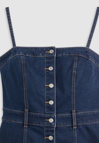 Vestido de mezclilla en un tono azul oscuro, con tirantes ajustables, frente de botones con herrajes plateados y detalles de costura destacada.