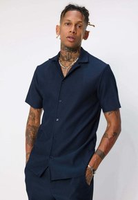 Chemise à manches courtes bleu marine avec un motif de rayures texturé et un col. Dotée de boutons foncés et d'une coupe décontractée.