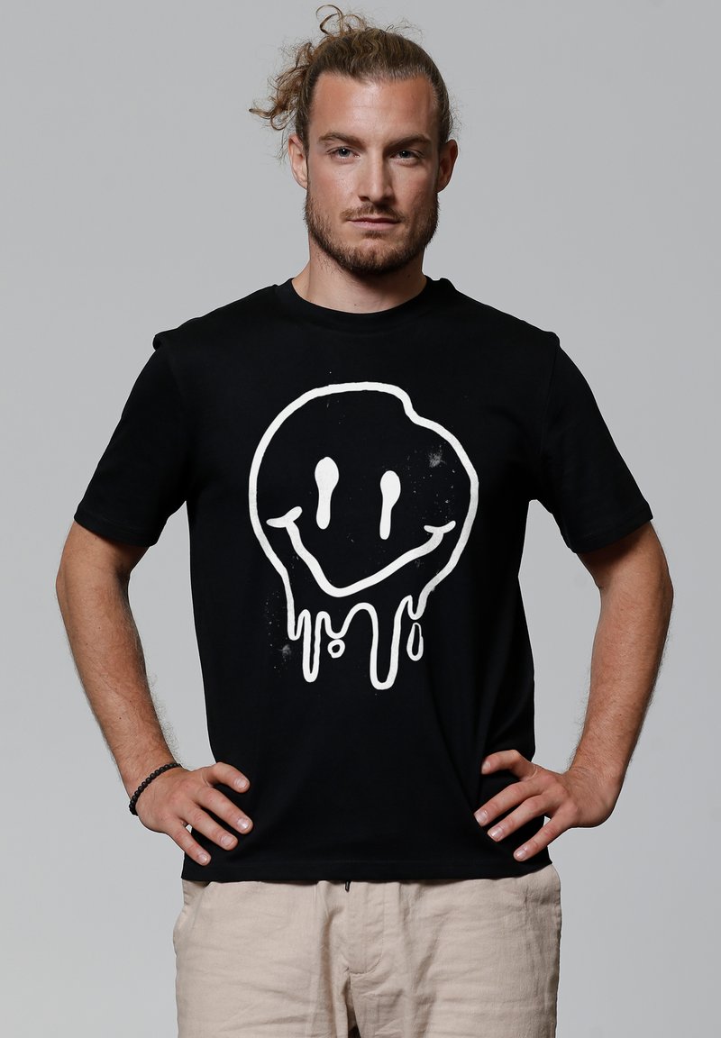Zwarte katoenen t-shirt met korte mouwen, voorzien van een groot, druipend wit glimlachend gezicht grafisch ontwerp aan de voorkant.