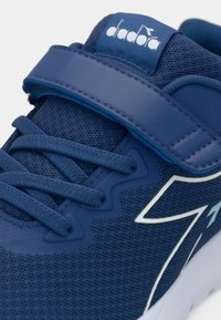 Chaussure de sport bleue avec une finition texturée, un bout arrondi et des accents blancs. Comprend des lacets et une sangle auto-agrippante pour le maintien.