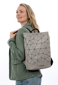 Šedý batoh s geometrickým vzorem, černými akcenty a horním úchopem, s hladkou strukturou a obdélníkovým tvarem, nošený na zádech.