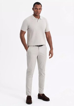 Vaaleanharmaa neulepolo, slim-fit vaaleat housut, tummanruskeat kengät; tekstuurinen kangas, lyhyet hihat, minimaalinen muotoilu kauluksella.
