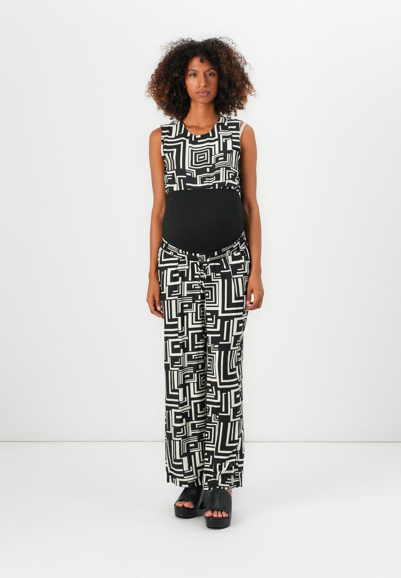 Svart-hvitt mønstret jumpsuit med ermeløs topp og vide bukser, med geometriske design og svart midje. Svart platåsandaler.
