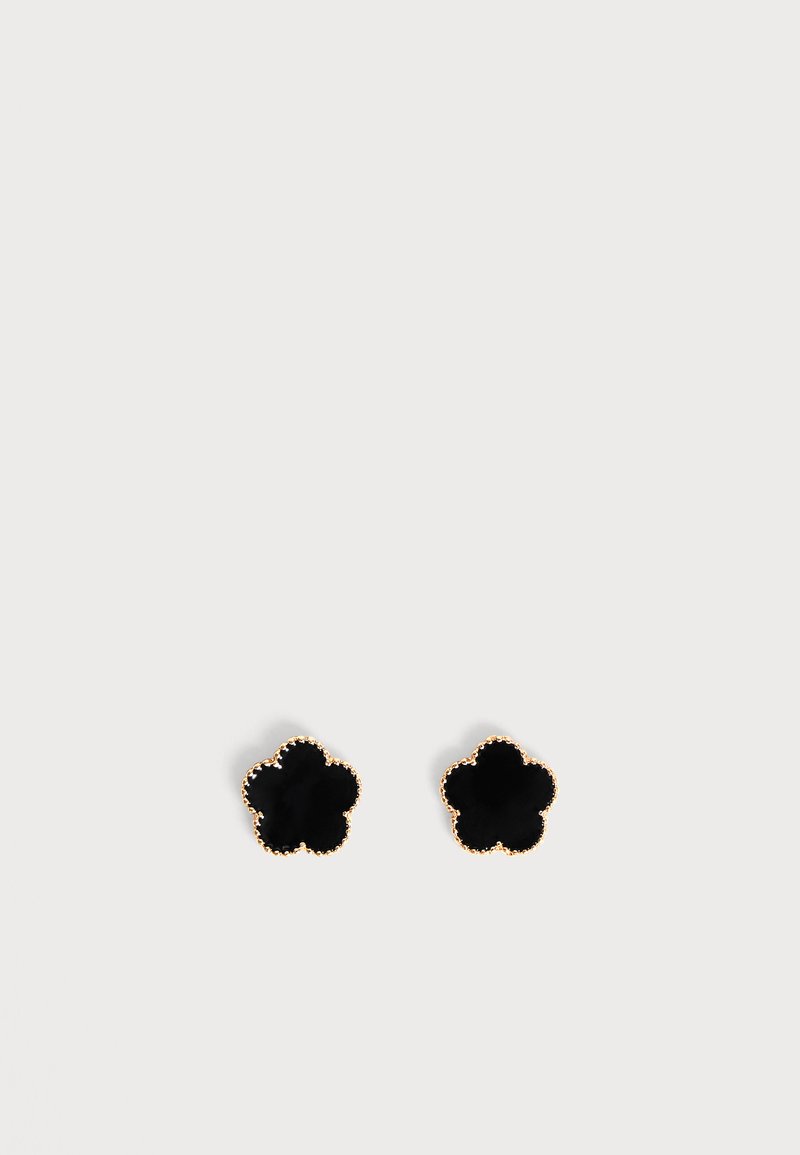 Boucles d'oreilles clous en forme de fleur noire avec bords perlés dorés sur fond blanc.