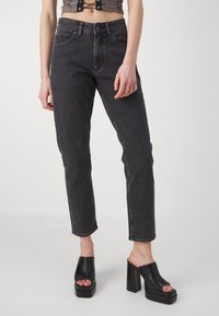 Black high-waisted jeans with a straight leg cut, featuring front pockets and a faded wash, paired with chunky black platform sandals.