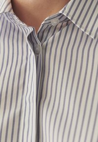 Chemise en coton à rayures verticales blanches et marines, avec col classique, fermeture boutonnée et texture lisse. Vue en gros plan.