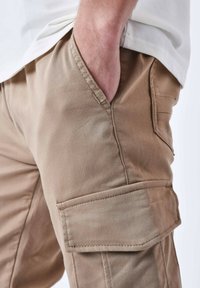 Pantaloni cargo beige realizzati in cotone resistente, con tasche laterali, una vestibilità comoda e dettagli di cucitura visibili per una maggiore durata.