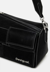 Czarna skórzana torba o strukturalnym wzornictwie, z zamkiem błyskawicznym, przednią kieszenią i srebrnym okuciem. Nazwa marki "Desigual" jest wytłoczona.
