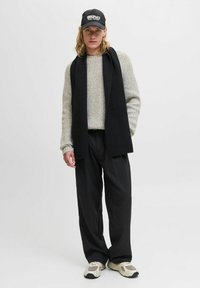 Suéter de punto en gris claro, bufanda de canalé negra, pantalones negros de rayas verticales y zapatillas crema con acentos grises. Gorra negra con logo blanco.