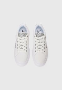 Weiße Sneaker mit einer glatten Lederoberfläche, silbernen Glitzerakzenten auf der Zunge und weißen Schnürsenkeln; Gummisohle mit minimalem Profil.