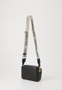 Svart lærcrossbody-veske med rektangulær form, med et kremfarget stropp merket "KARL LAGERFELD" og detaljer i gull.